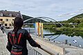 Person in schwarzer Motorradkleidung mit rotem Helm blickt auf Fluss, Brücke und Gebäude bei bewölktem Himmel.