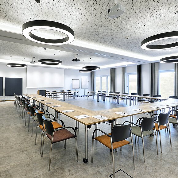 Konferenzraum mit U-förmiger Tischanordnung, Stühlen, moderner Beleuchtung und Präsentationsflächen.