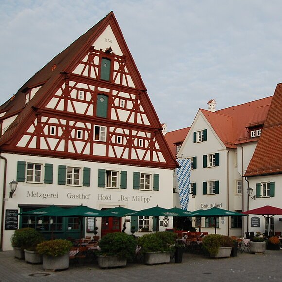 Traditionelle Fachwerkhäuser mit Außenbestuhlung und Sonnenschirmen an einem gepflasterten Platz.